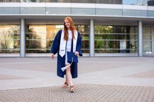 BYU student wearing cap and gown walks confidently towards camera.