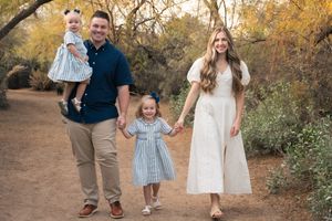 A family walks together on a dirt path surrounded by autumn foliage during golden hour in Mesa, Arizona.