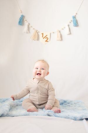 Baby in light colored outfit sitting on blue blanket with festive tassel banner decoration in Mesa, Arizona.