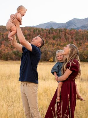 Family playing and lifting child in golden field with mountains in background in Provo, Utah.