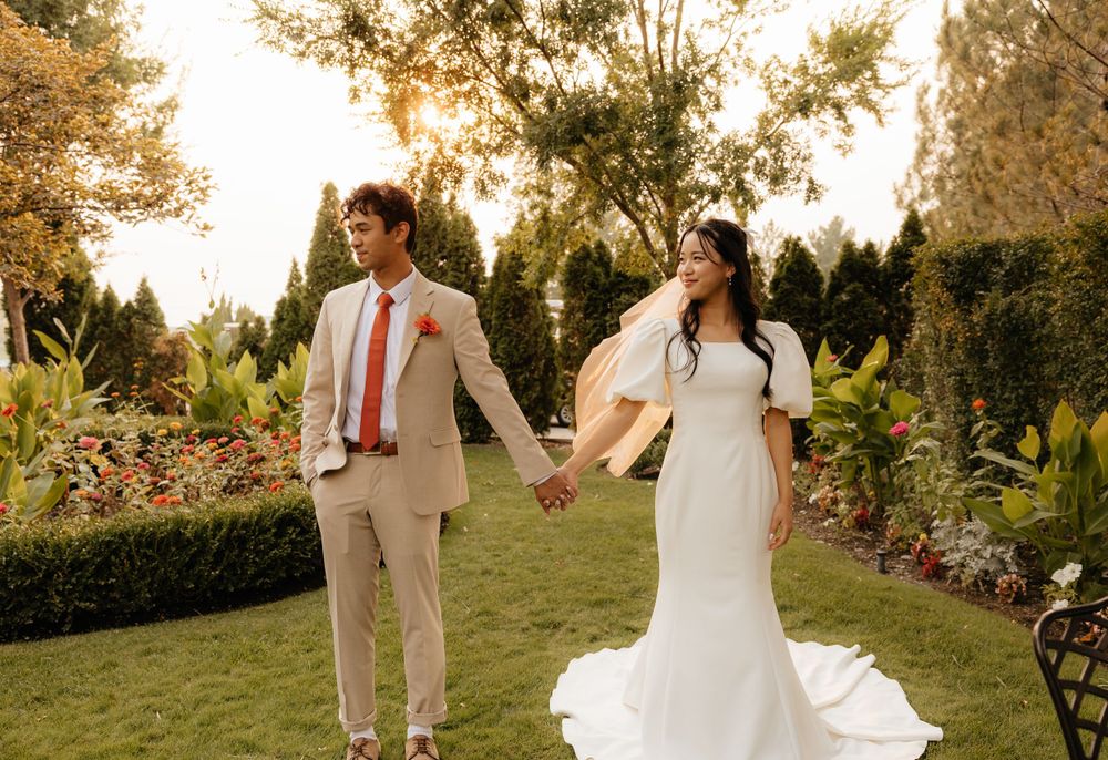 Bride and groom holding hands walking through garden at sunset on wedding day.
