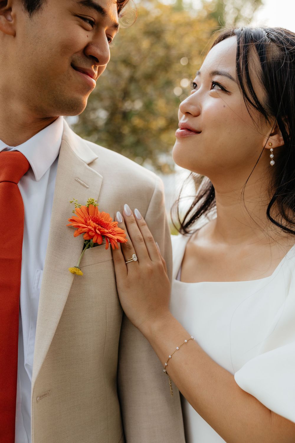 Bride gazing at groom wearing orange tie and gerbera daisy boutonniere.