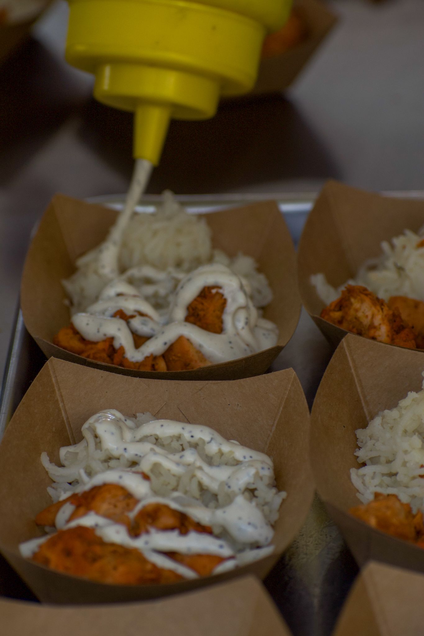 White sauce being drizzled over breaded chicken in paper food containers.