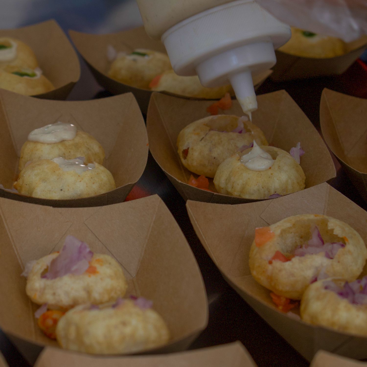 Close-up of pastries in paper boats being drizzled with white sauce.