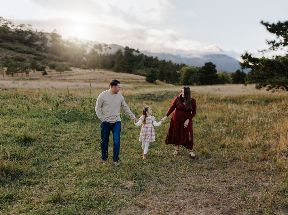 Three people walk hand in hand through a mountain meadow at sunset. Colorado Springs Photographer.