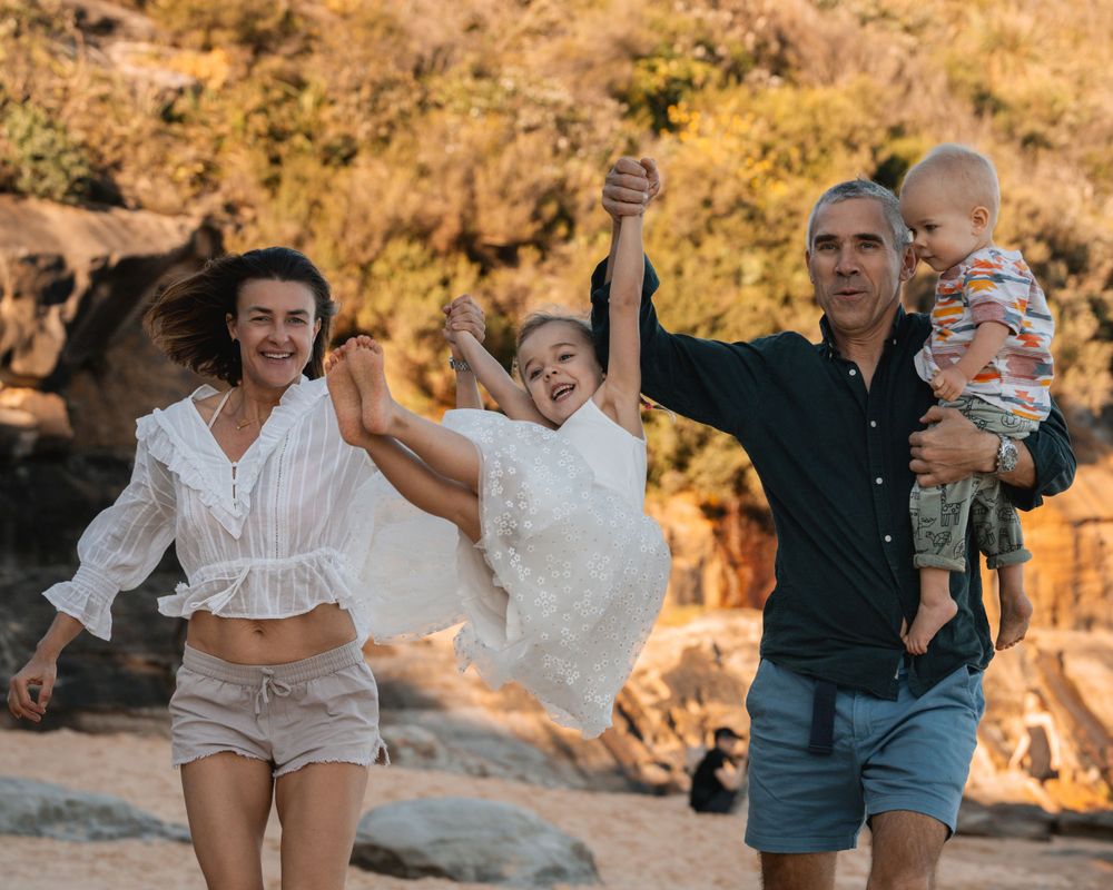 dad and mom runs and lifts up daughter at the beach in Sydney during a family photoshoot