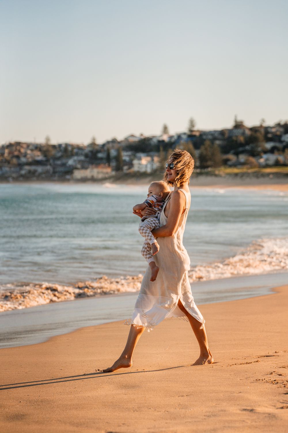 mom holds toddler son and walks towards the water during a family photoshoot