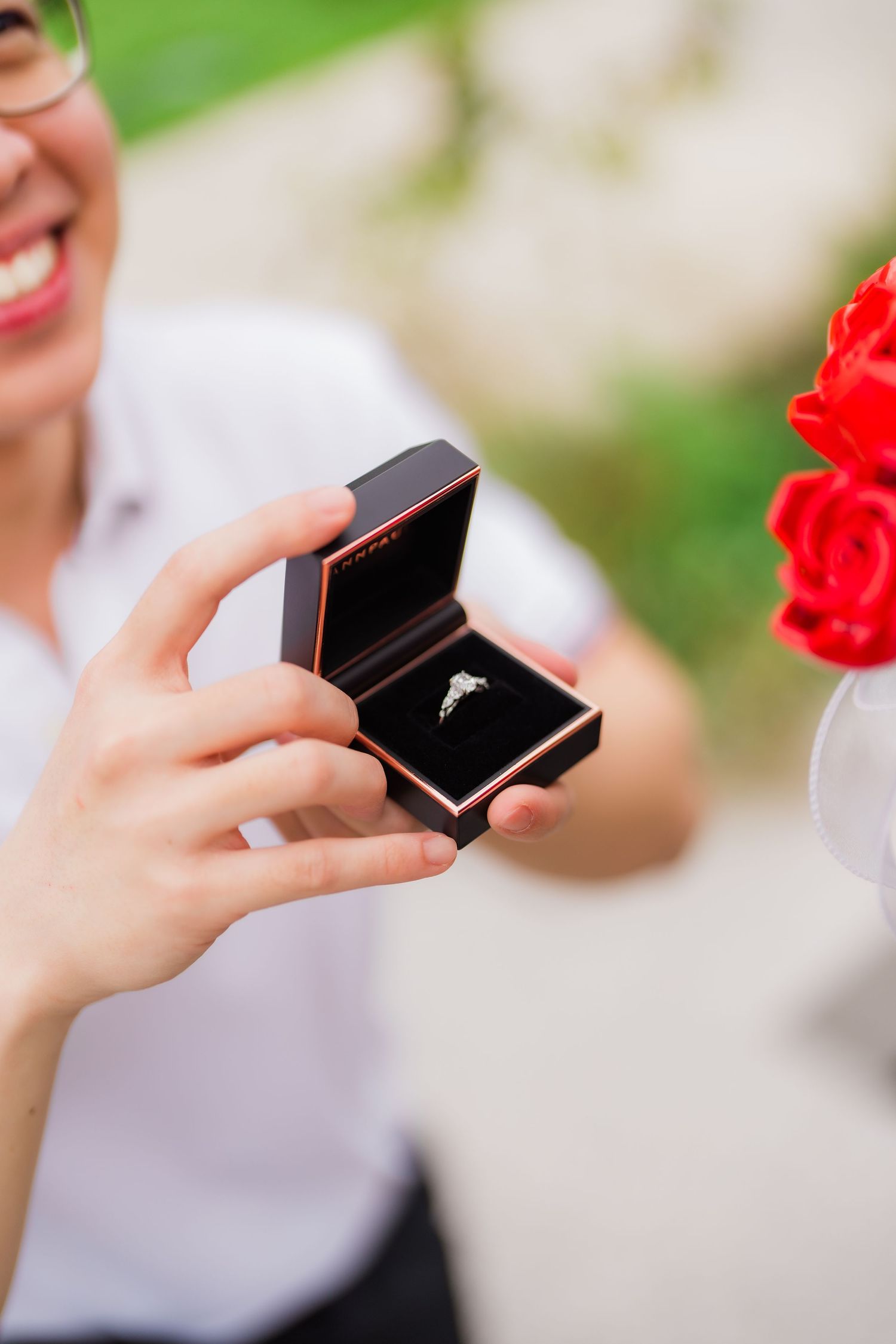 Close up of hands holding an engagement ring box with a sparkling diamond ring inside.