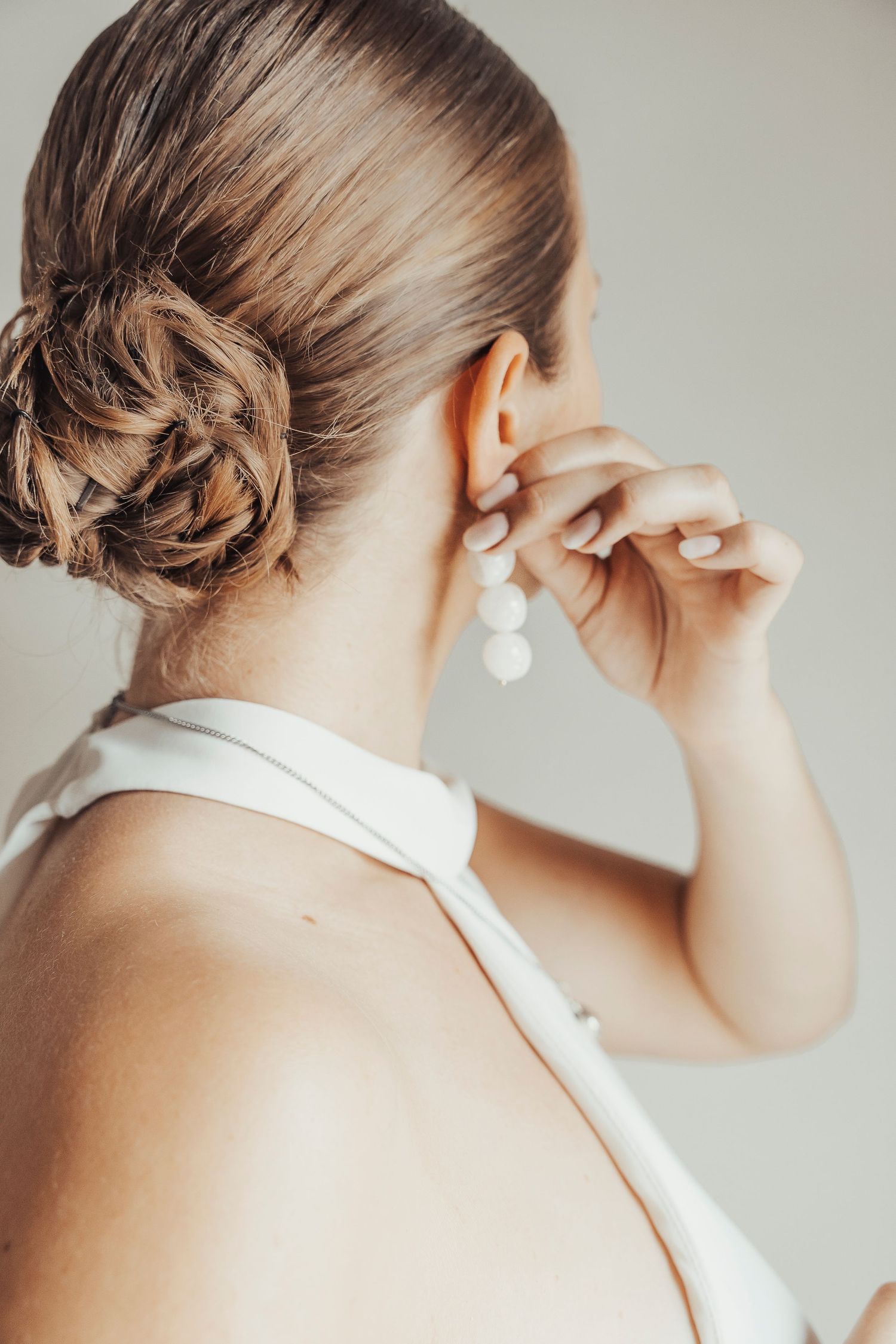 Close up of elegant bridal hairstyle and pearl earring being put on.