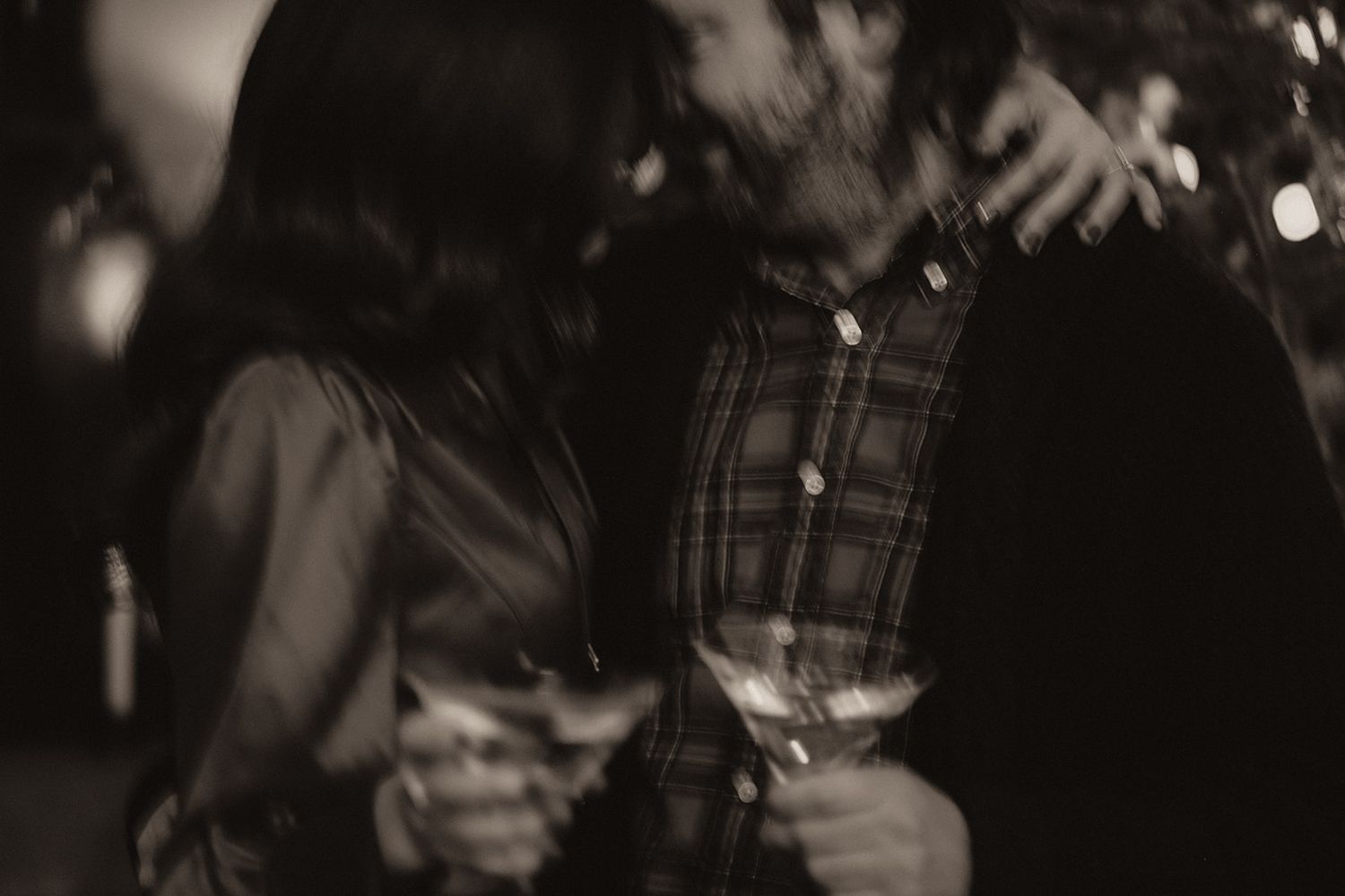 Blurry black and white photo of couple holding wine glasses at evening gathering.