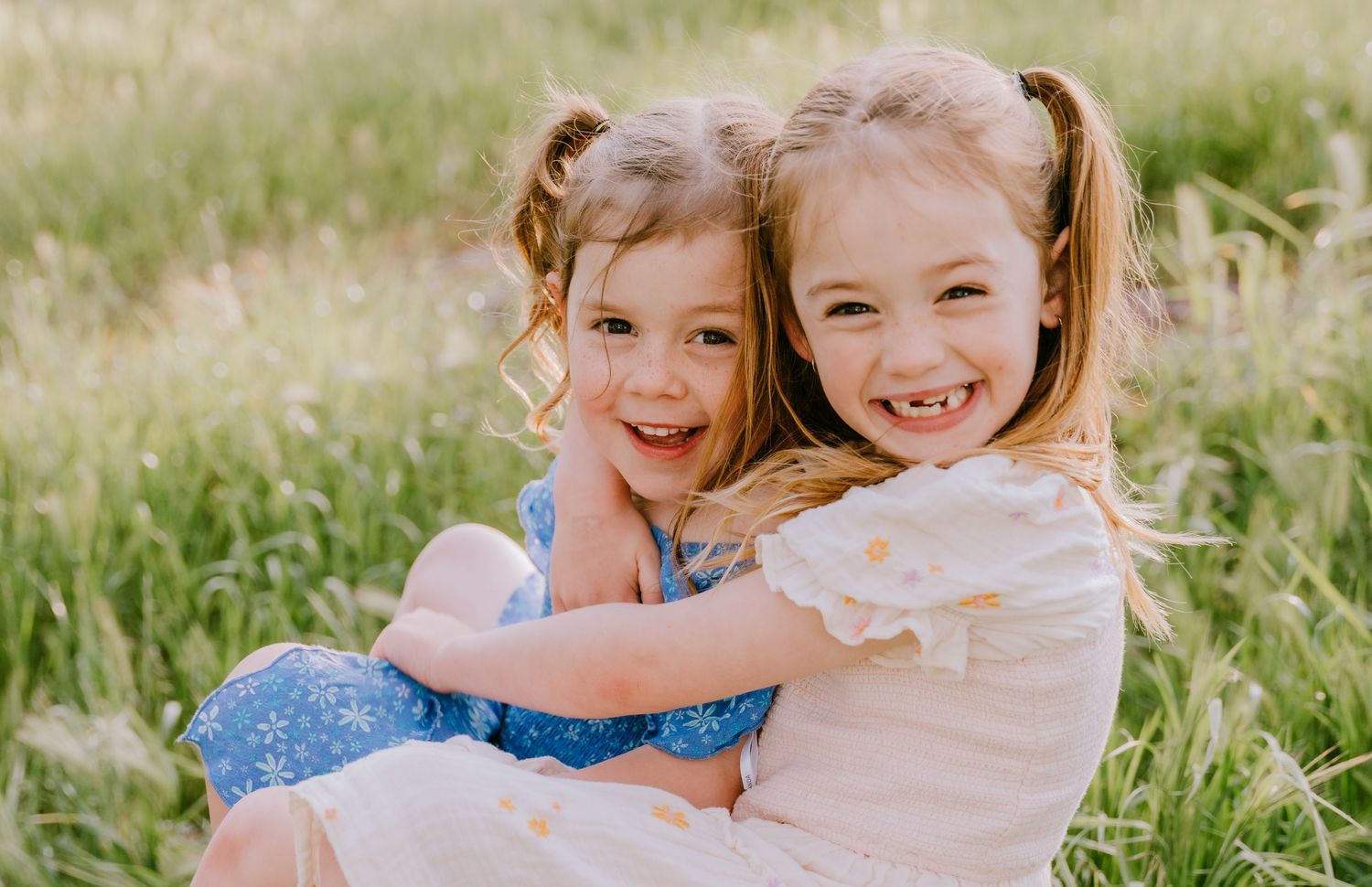 Two young children hugging and laughing together in a sunny field.
