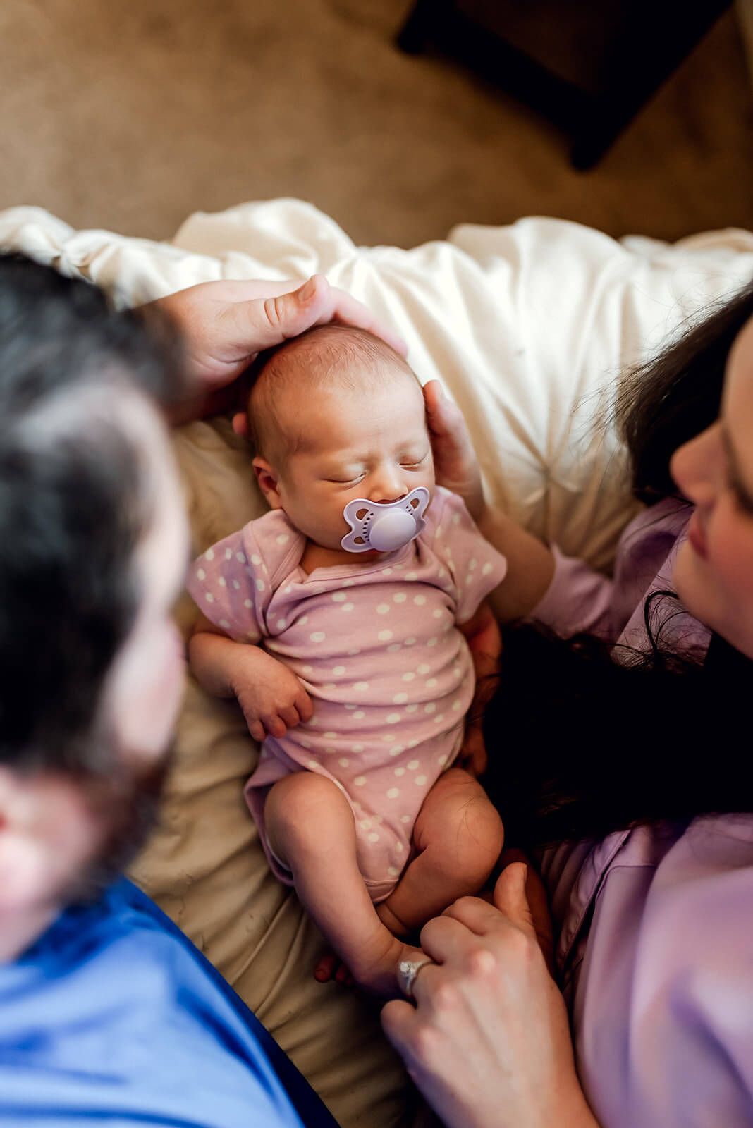 Peaceful sleeping newborn baby with pacifier surrounded by family on bed.
