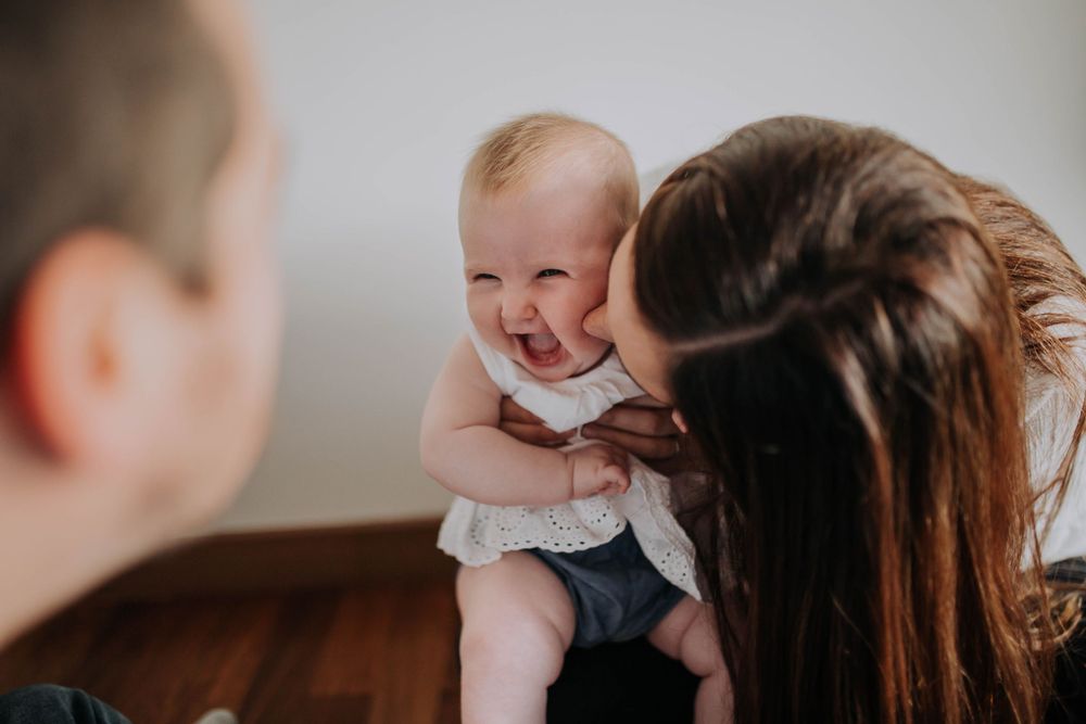 Happy baby laughing during playtime with adults in natural indoor lighting.