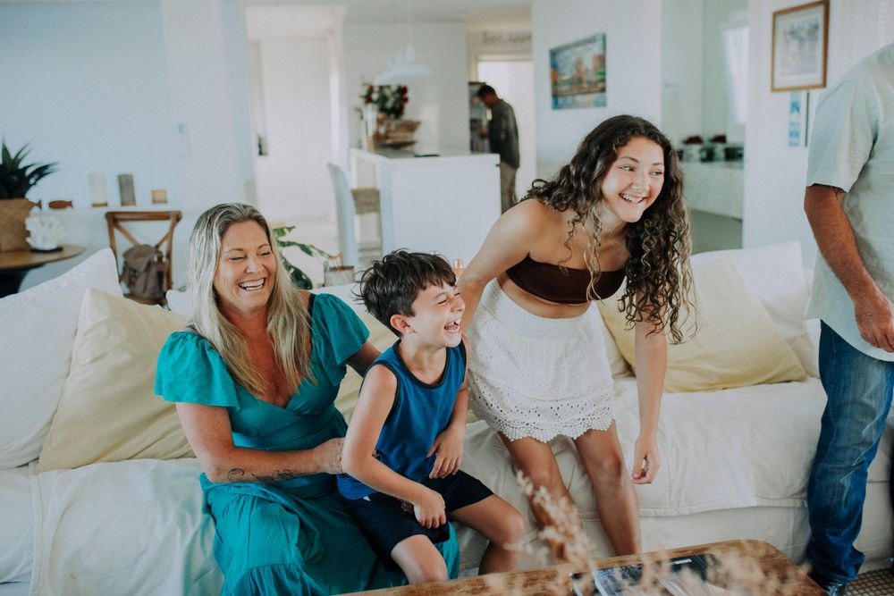 Joyful group laughing together on a white couch in a bright living room interior.