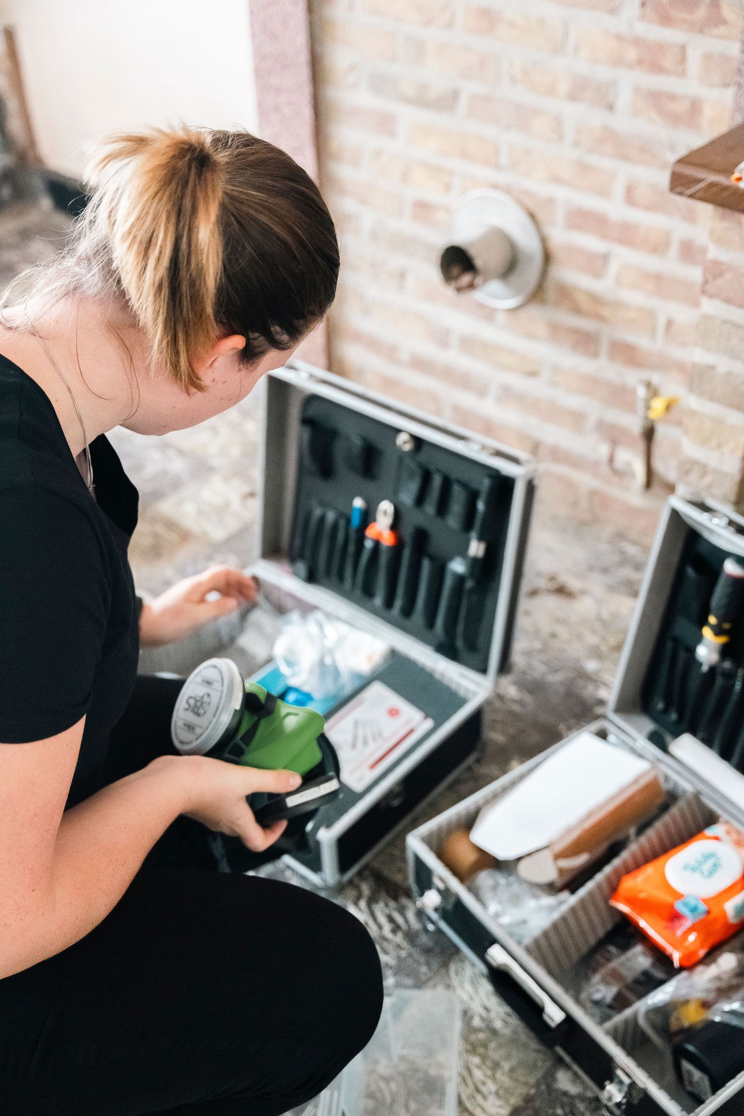 Forensic investigator examining evidence kits with tools and supplies against a brick wall background.