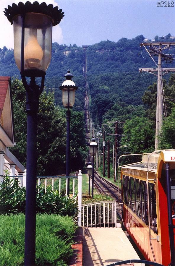 Vintage funicular railway track with ornate lamp posts winding up a forested hillside.