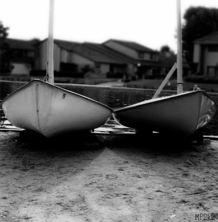 Two small white boats resting upside down on a beach in black and white.