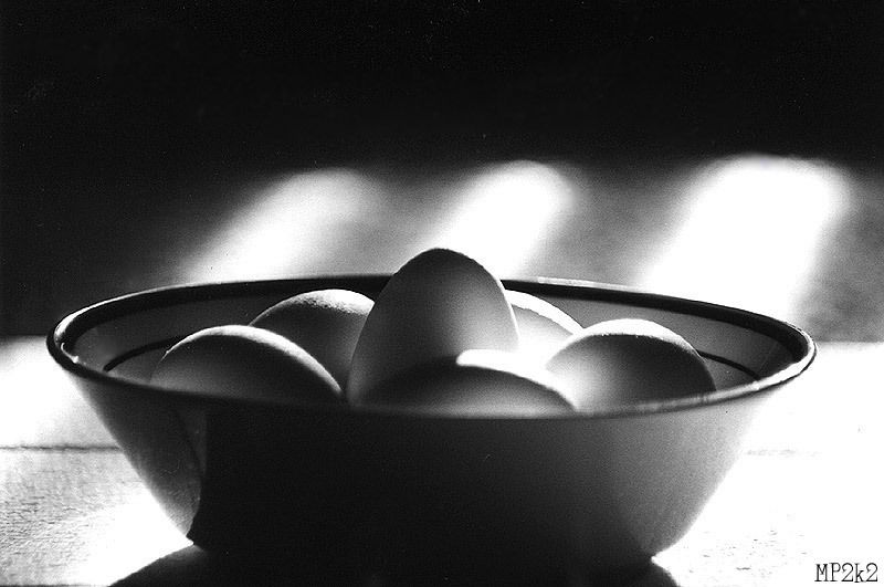 Dramatic black and white photograph of eggs in a ceramic bowl with strong lighting.