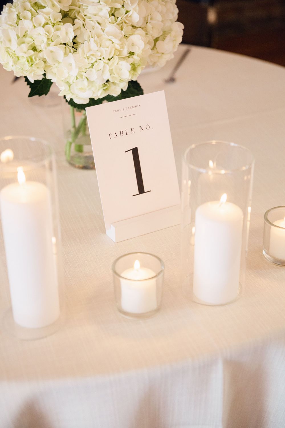 Elegant table setting with white hydrangeas, candles and table number one card.