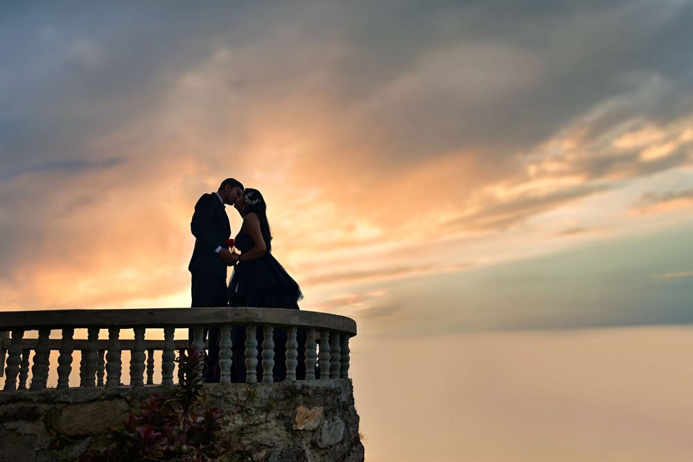 Silhouetted couple embraces on a stone balcony against a dramatic sunset sky.