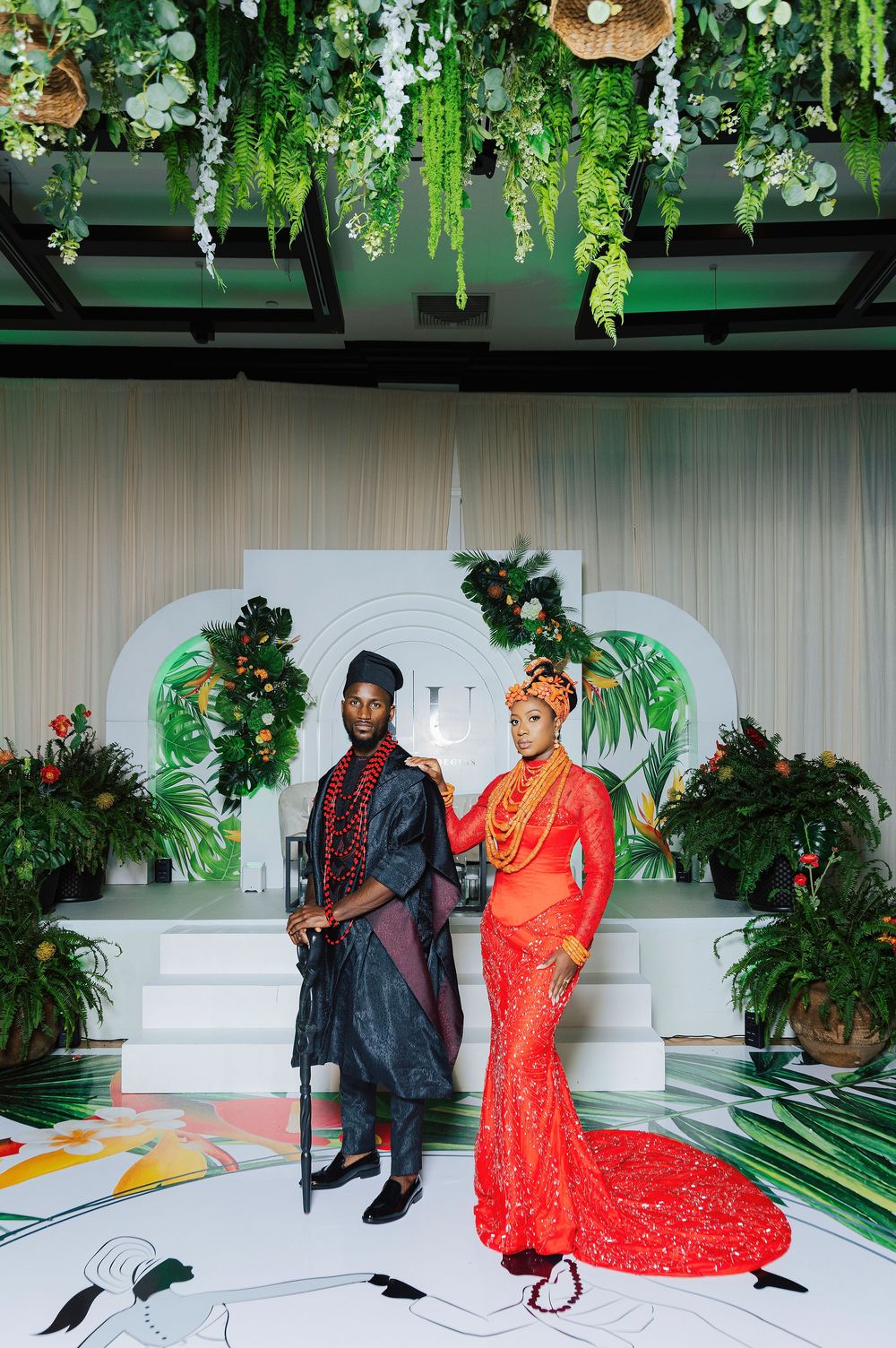 Nigerian couple in traditional wedding attire posing at elegant tropical-themed ceremony with lush greenery decor.