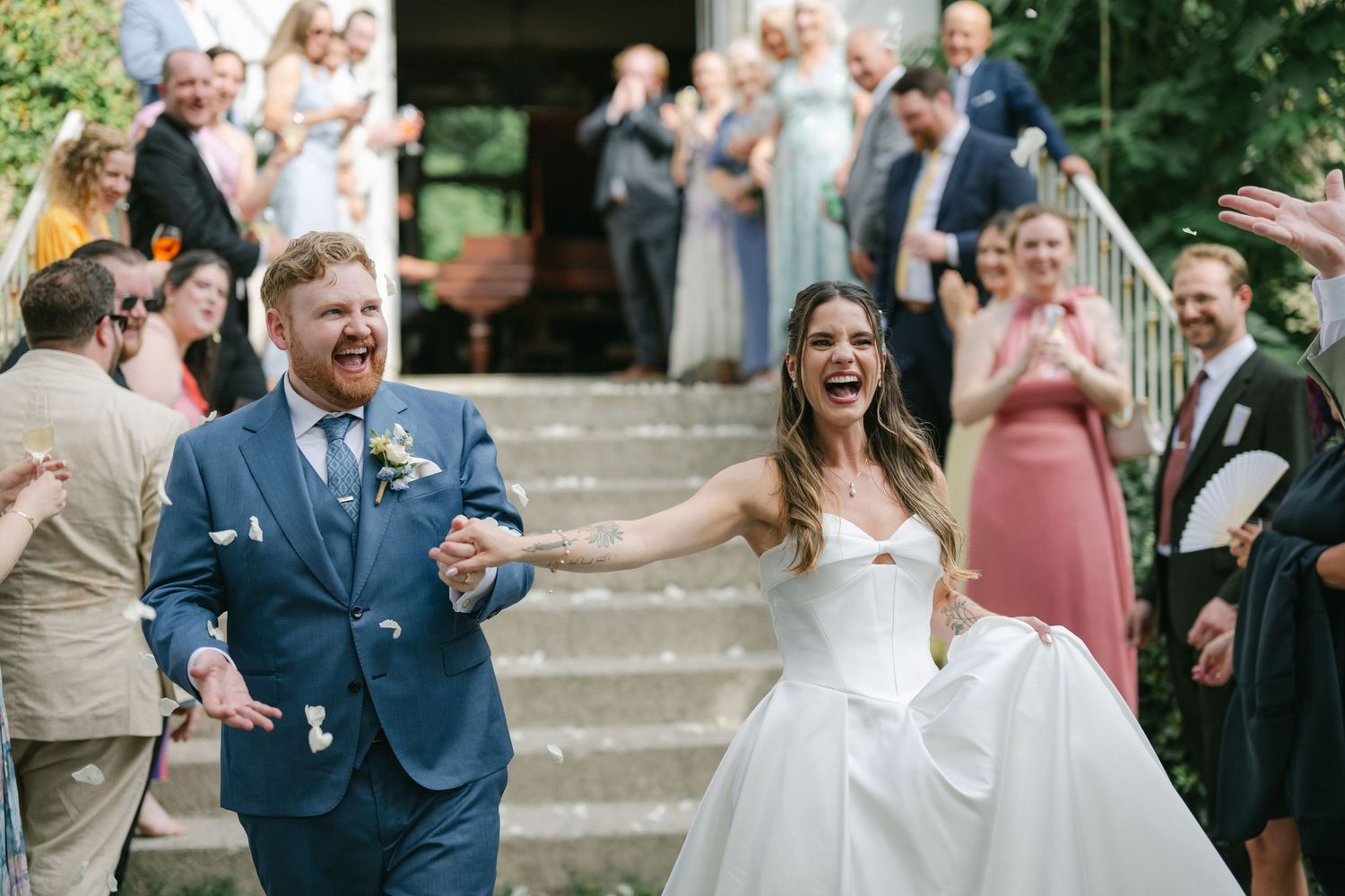 Joyful newlyweds exit wedding ceremony as guests celebrate with confetti on outdoor steps.