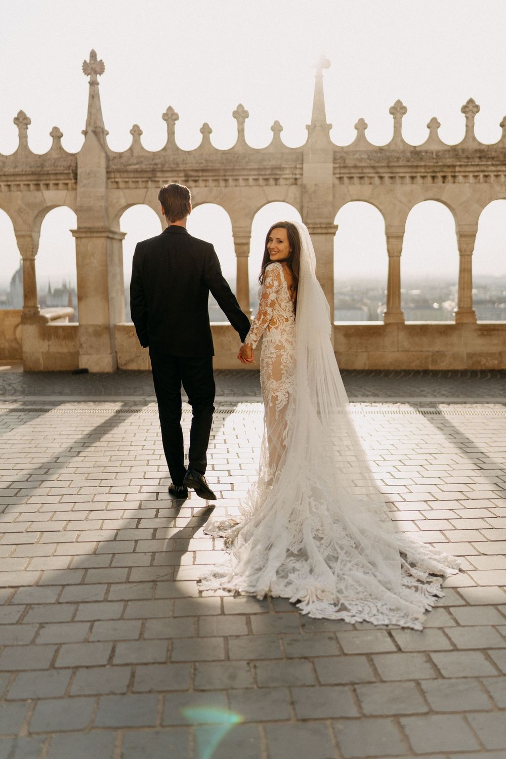 Bride and groom holding hands on cobblestone terrace at Fishermans Bastion Budapest.