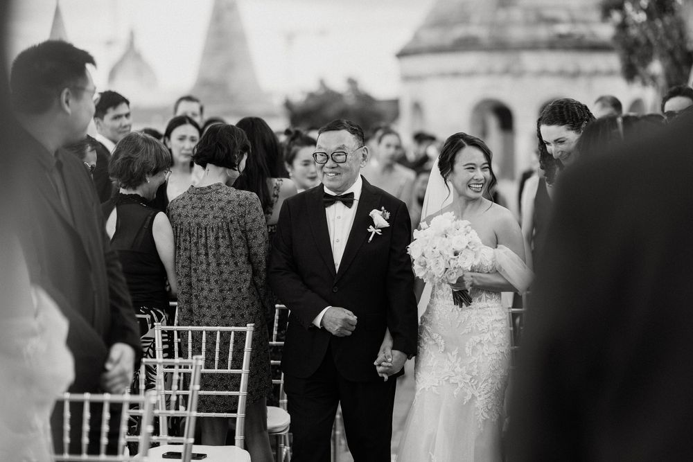 Black and white photo of bride walking aisle with father at outdoor wedding.