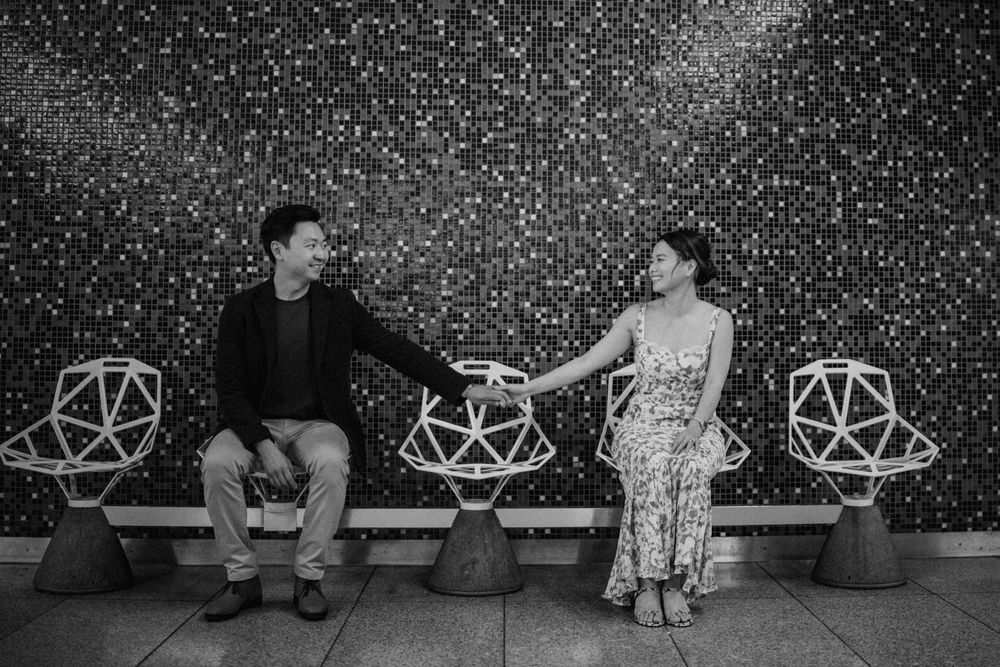 Black and white photo of couple laughing and holding hands on modern chairs.