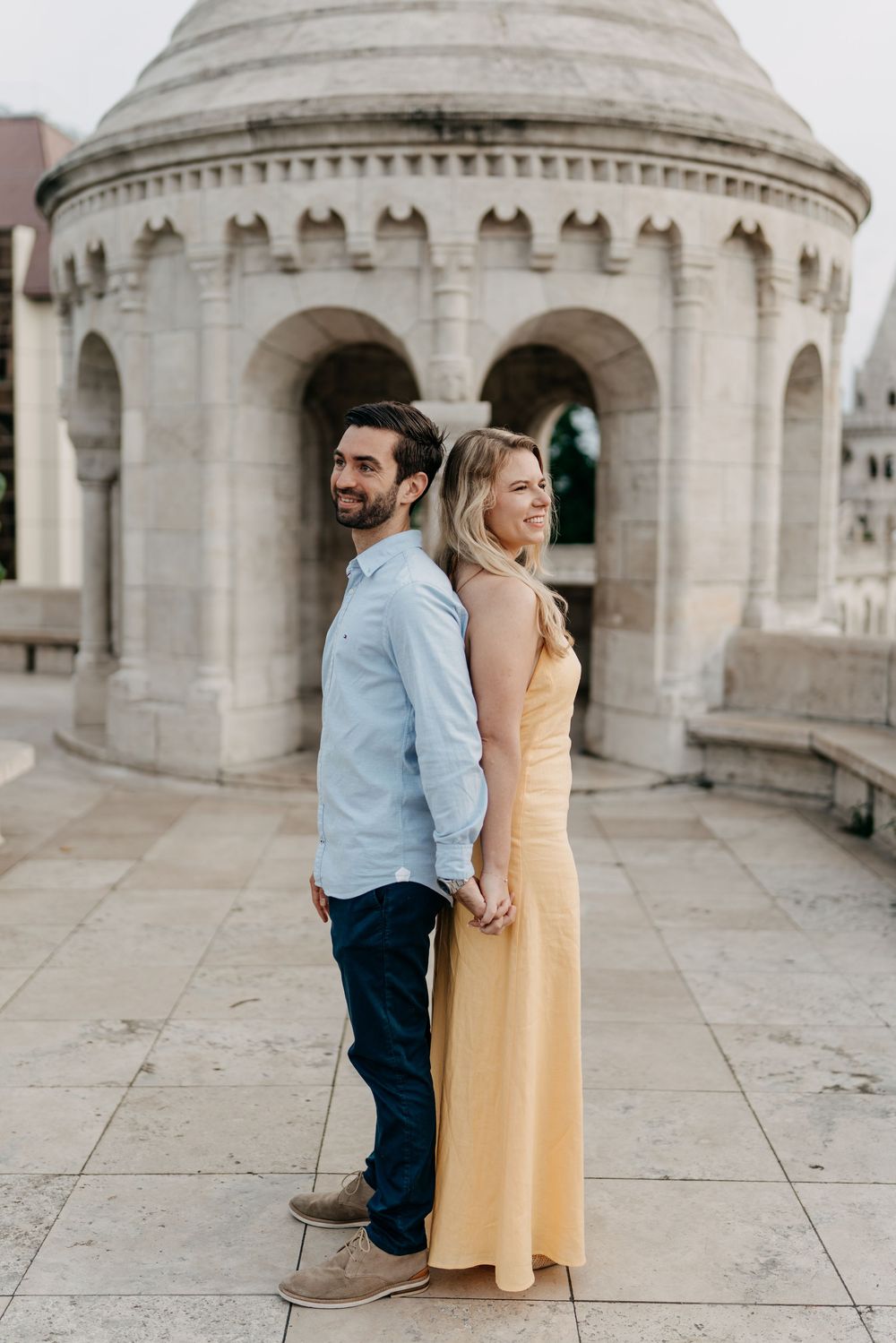 Couple holding hands back-to-back at Fisherman's Bastion Budapest in a yellow dress and blue shirt.