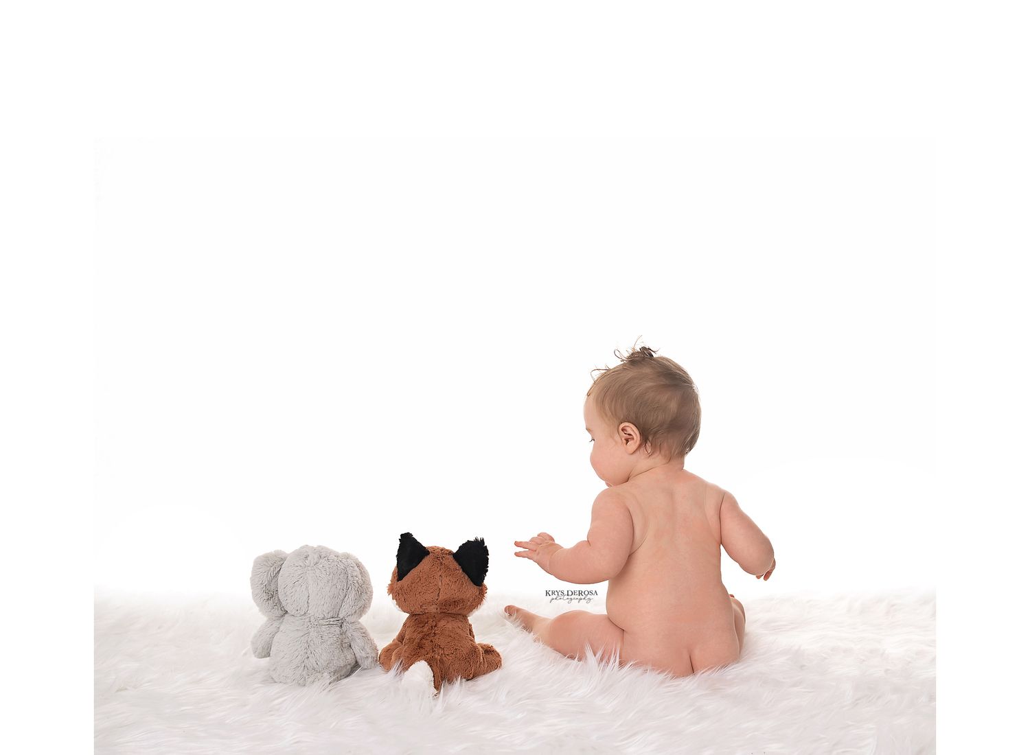 Baby sitting on white fur rug with gray elephant and brown fox stuffed animal toys.