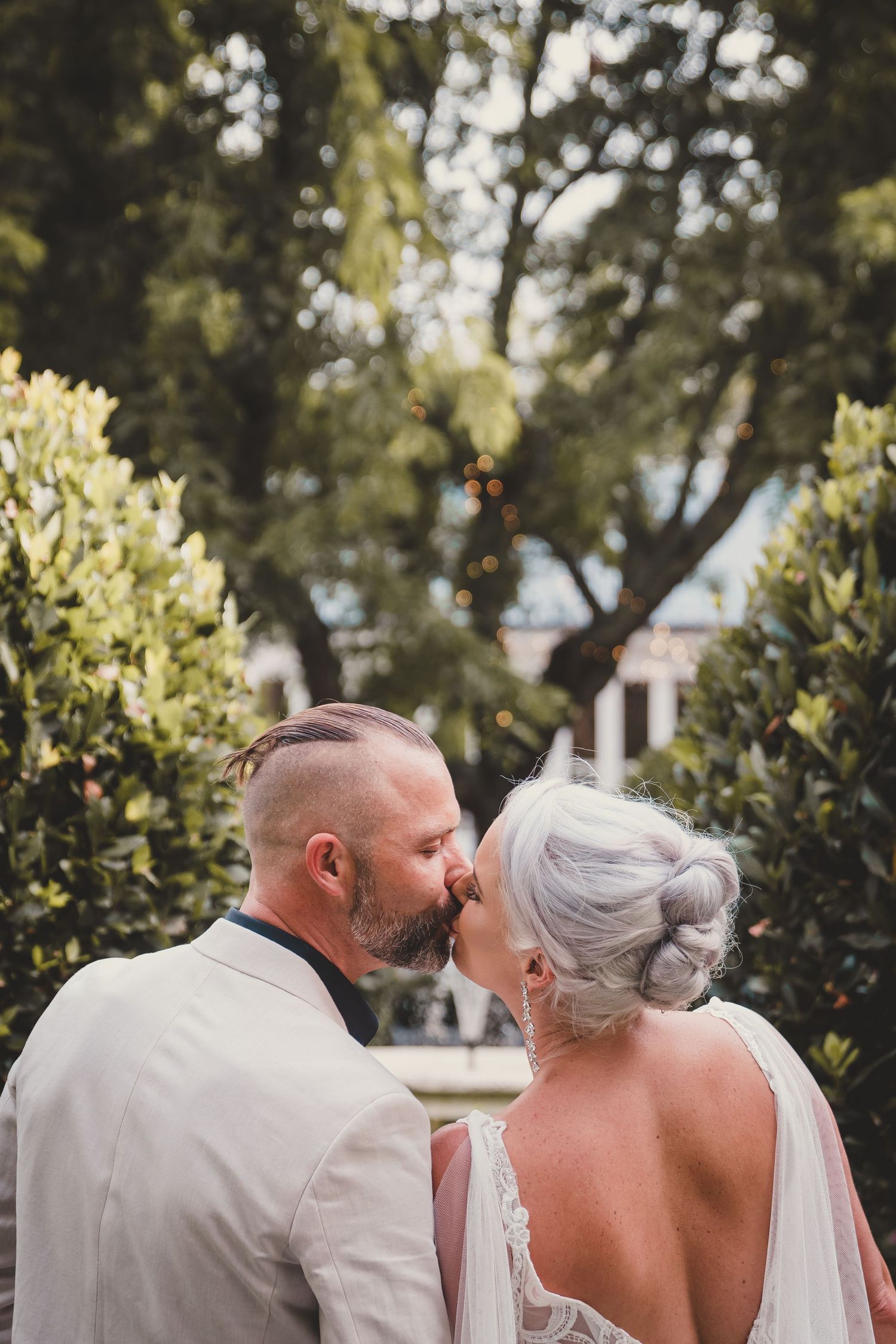 A bride and groom share a romantic kiss in a lush garden setting, with the bride wearing an elegant updo.