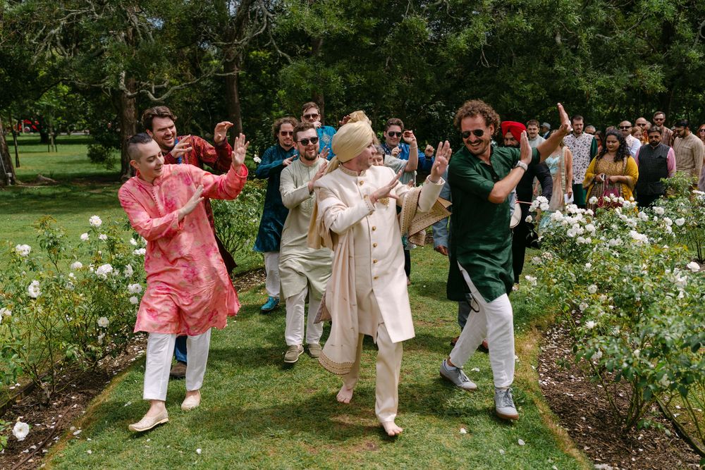 People in colorful traditional South Asian attire dancing joyfully outdoors in a lush green garden setting.