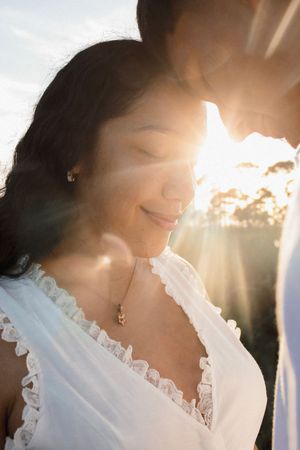 Woman smiling peacefully with eyes closed in golden sunset light wearing white lace dress.