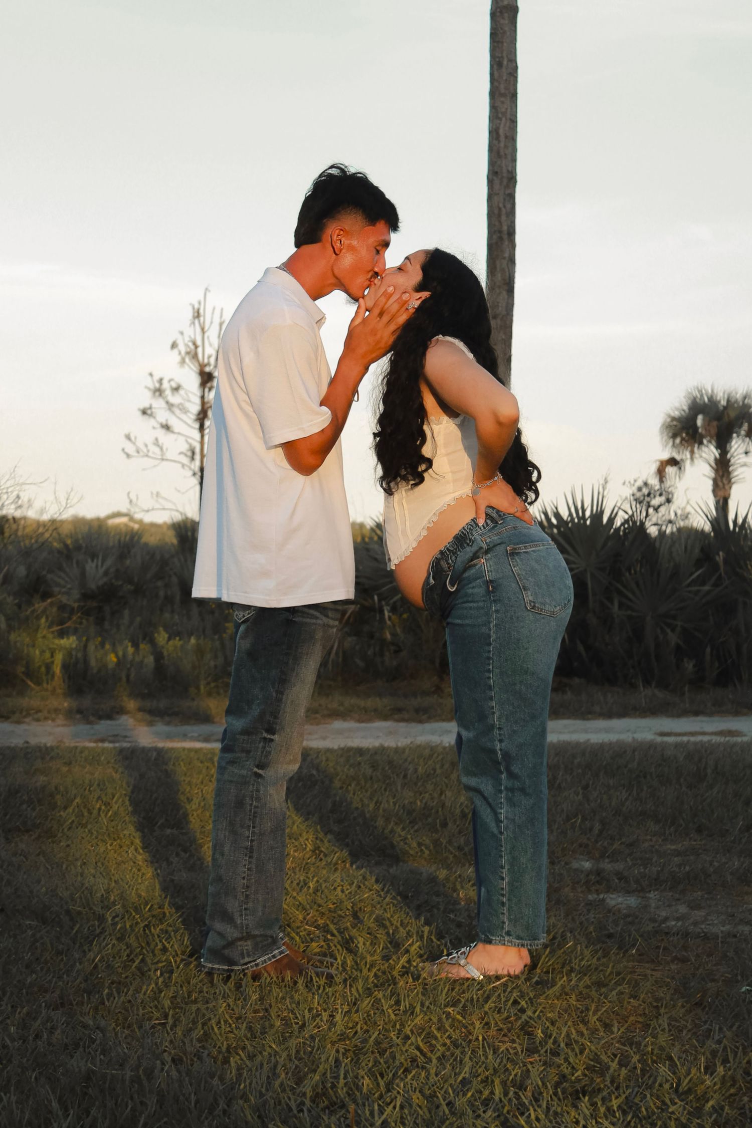 Young couple sharing a tender kiss outdoors at golden hour with palm trees in background.