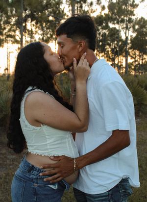 Couple sharing passionate kiss outdoors in pine forest during warm golden sunset.