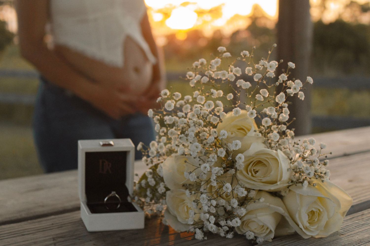 White rose bouquet with baby's breath and engagement ring box at golden sunset.