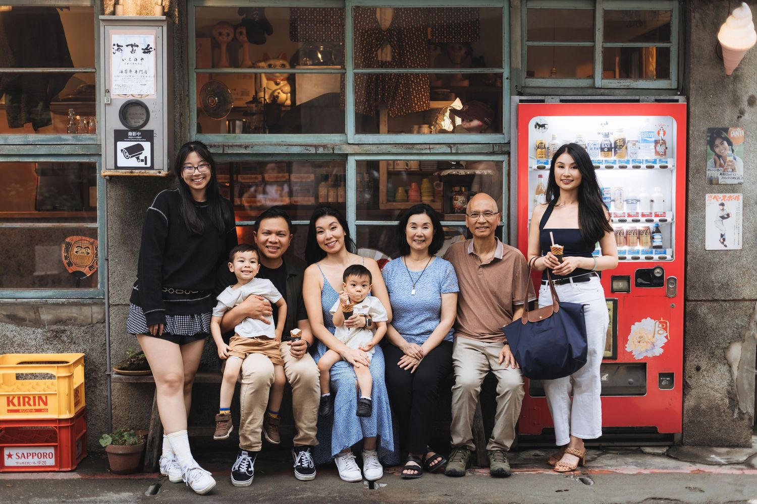 Multi-generational Asian family posing together outside a vintage shop with a red Kirin vending machine.