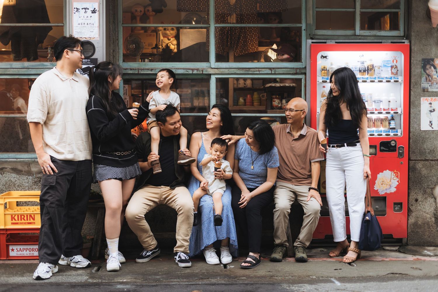 Multi-generational Asian family gathering outdoors near a red vending machine, laughing and bonding together.