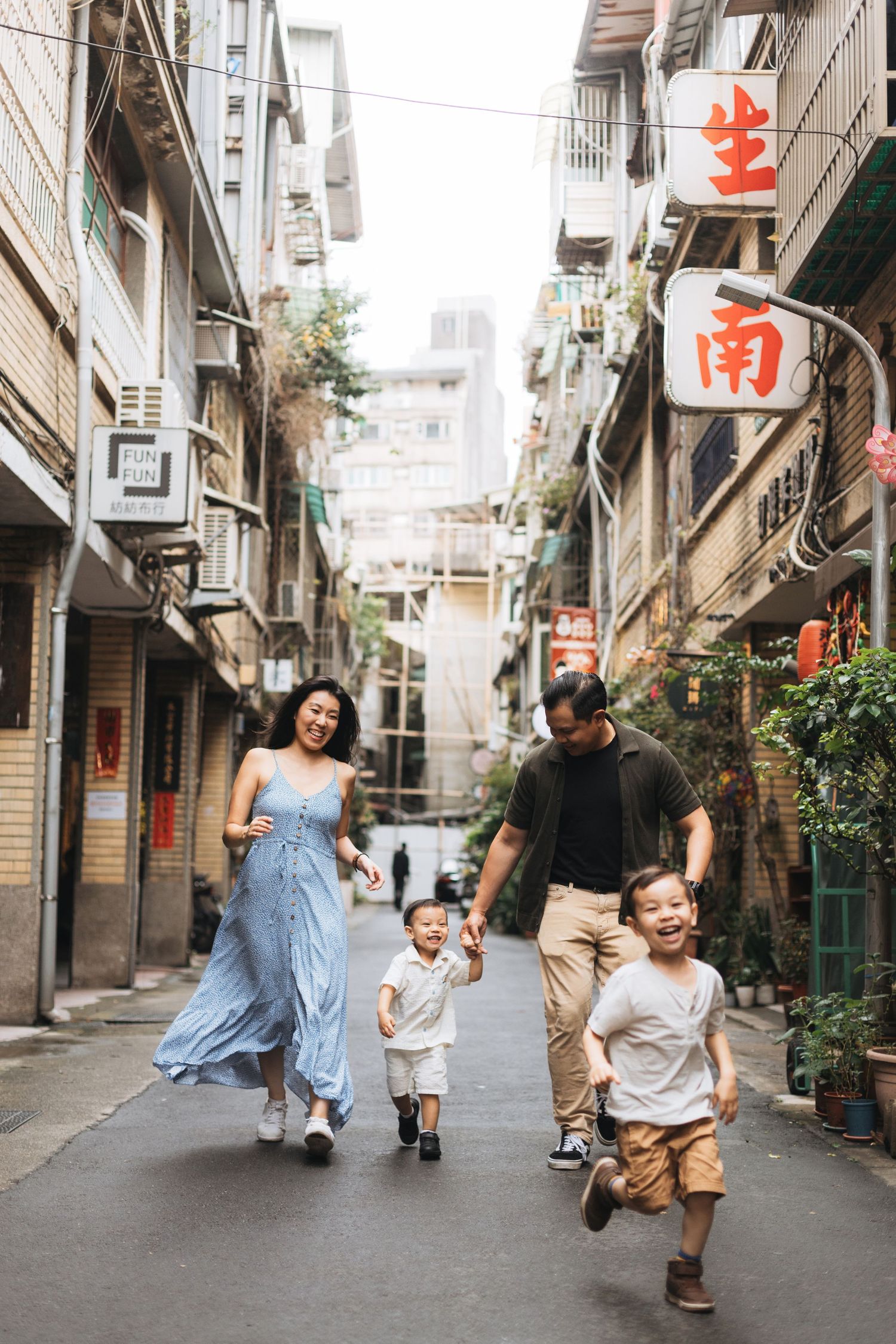 Happy Asian family walking together in a narrow urban alley with Chinese signage in Taiwan.