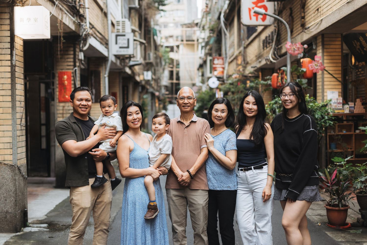Multigenerational Asian family posing together on a charming narrow street with traditional shophouses.