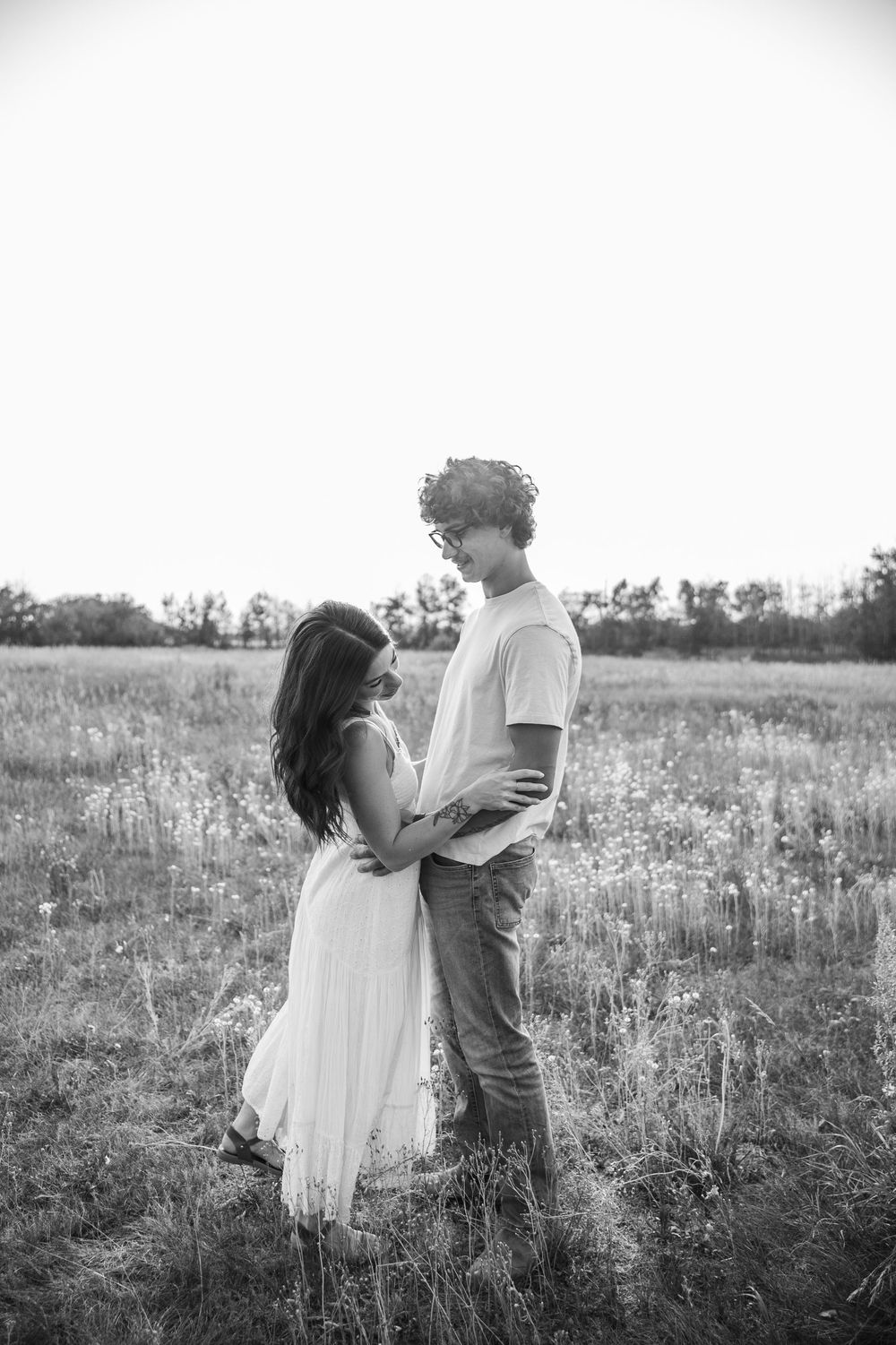 Black and white photo of a young couple embracing in a wildflower field, gazing at each other romantically.