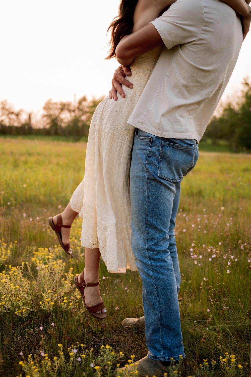 A romantic couple embracing in a wildflower meadow at golden hour, woman lifted off the ground.