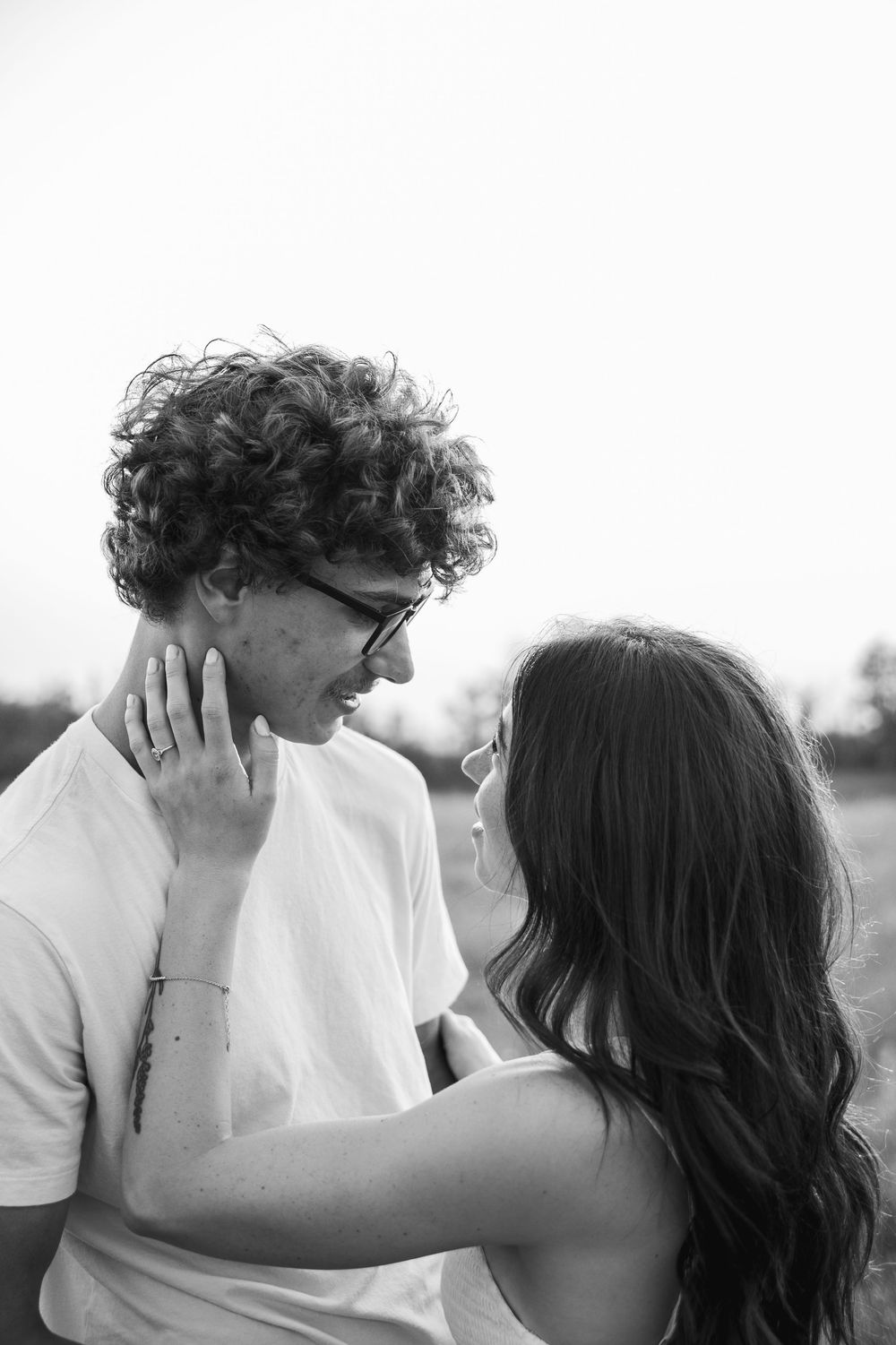Black and white photo of a young couple sharing a tender moment, woman touching mans face outdoors.