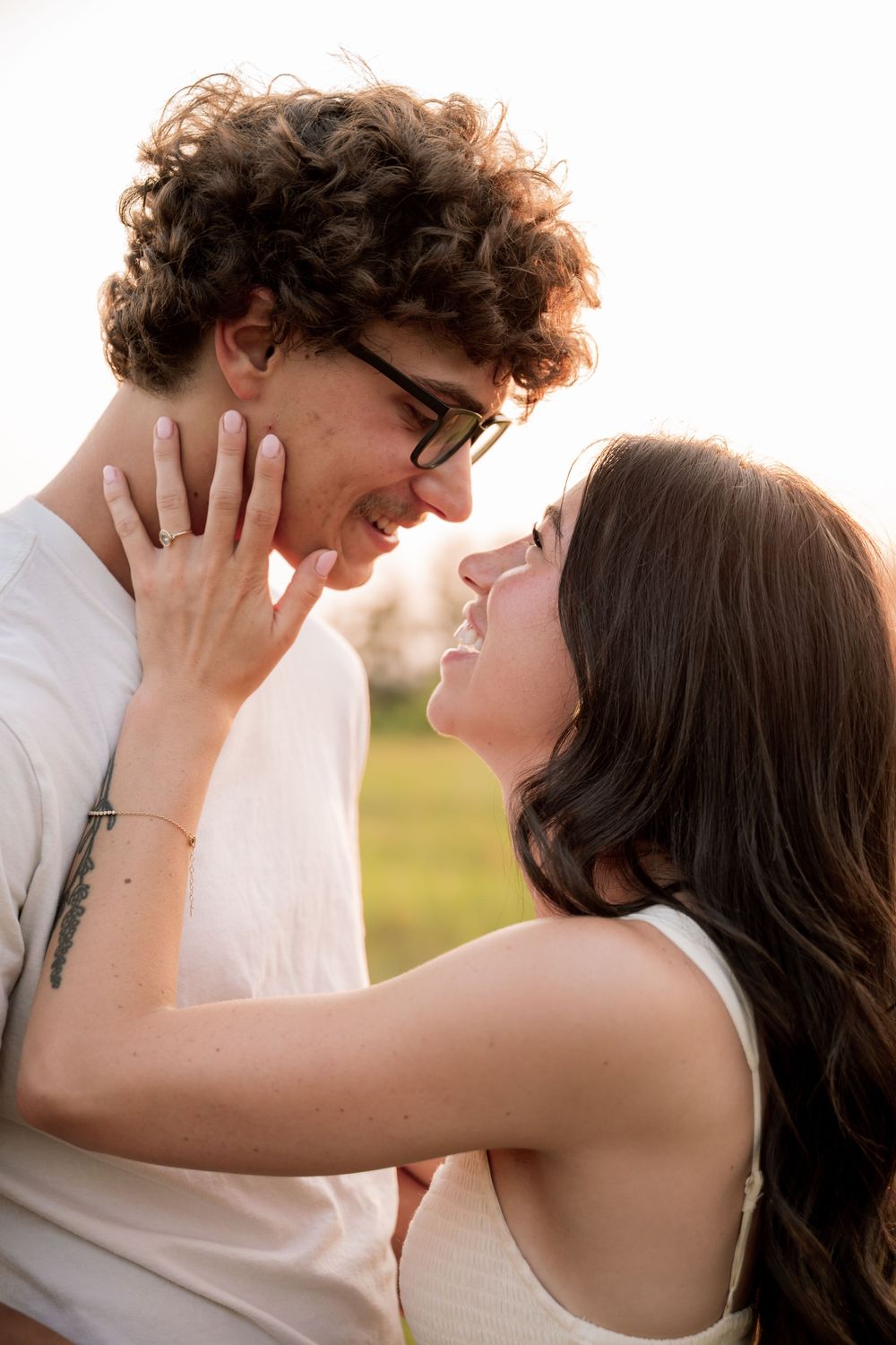 A young couple smiling and gazing at each other outdoors, sharing a romantic moment in a sunlit field.