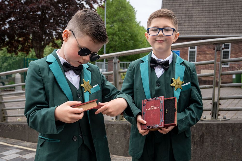 Two boys in green tuxedos with bow ties holding books and awards outdoors.