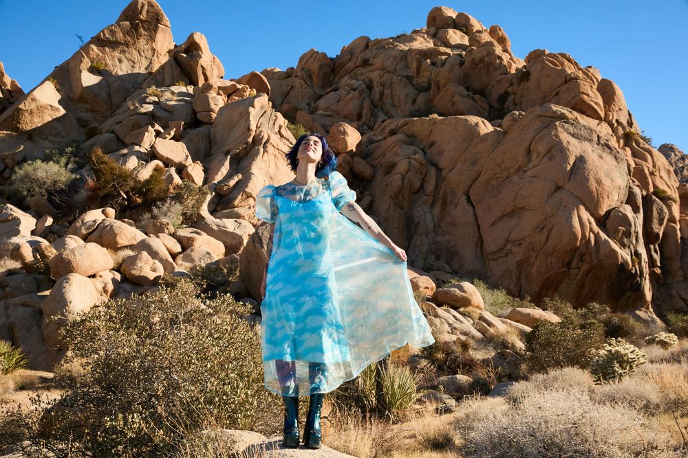 Woman in blue floral maxi dress poses among desert boulders in Joshua Tree, California.