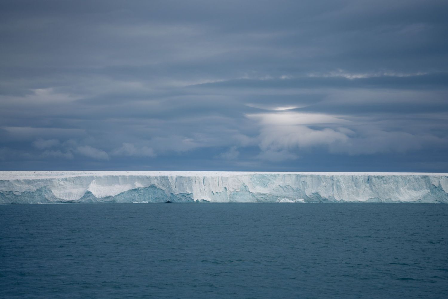 Longue barrière de glace de Bråsvellbreen sous une trouée lumineuse dans les nuages