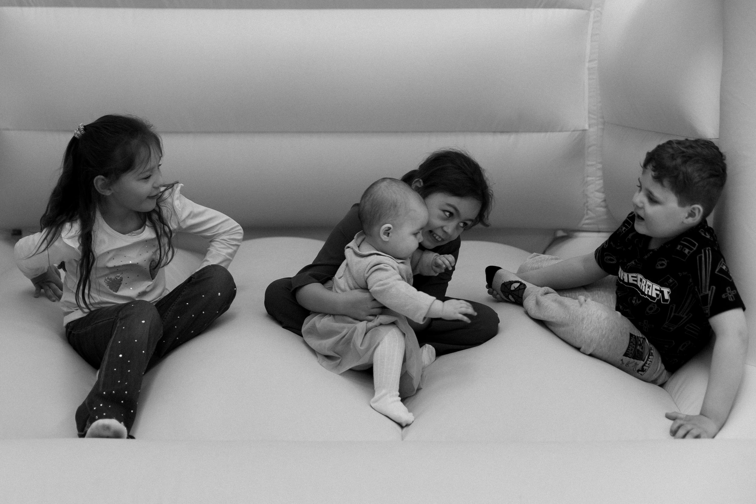 Black and white photo of four young children playing together on a white bouncy castle surface.