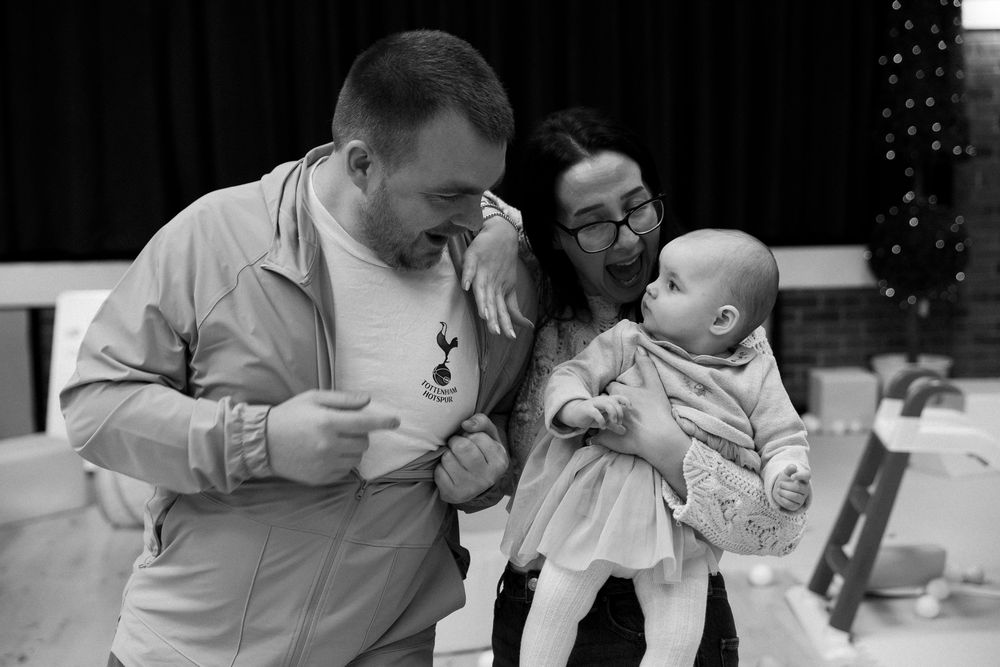 Black and white photo of a couple smiling at their baby at a birthday party indoor event.